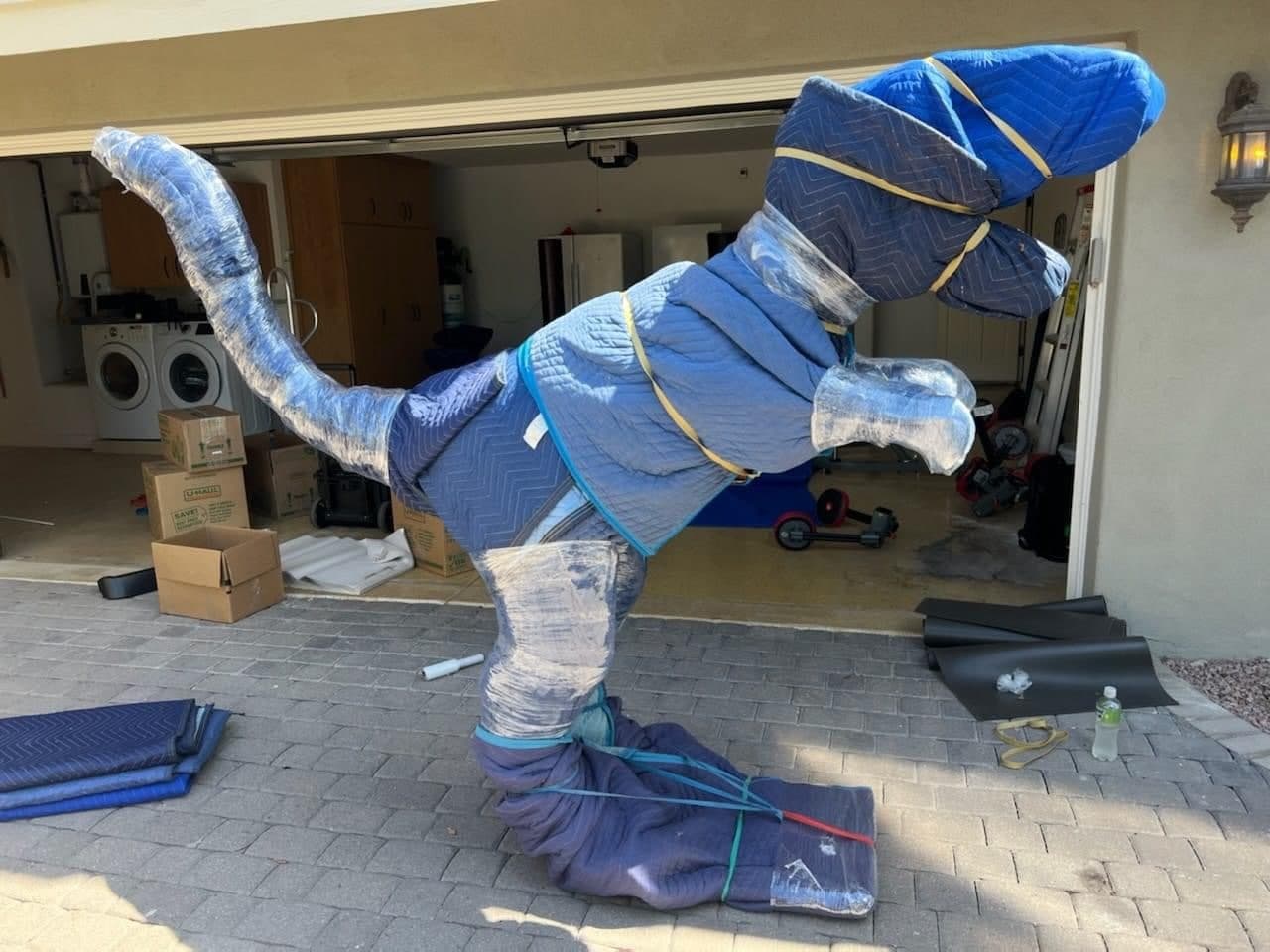 A large dinosaur statue carefully wrapped and padded in moving blankets for transport